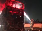 Petugas Dinas Pemadam Kebakaran dan Penyelamatan melakukan proses pembasahan pada bangkai Bus Gunung Harta yang hangus terbakar hingga menyisakan rangka di Tol Nganjuk